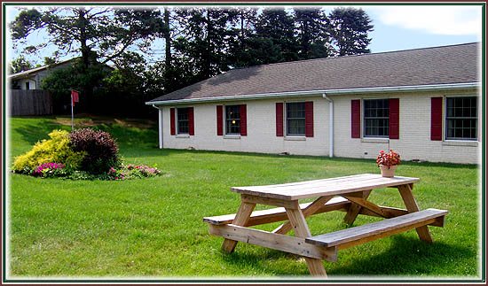 A house with red shutters and a picnic table on a grassy lawn.
