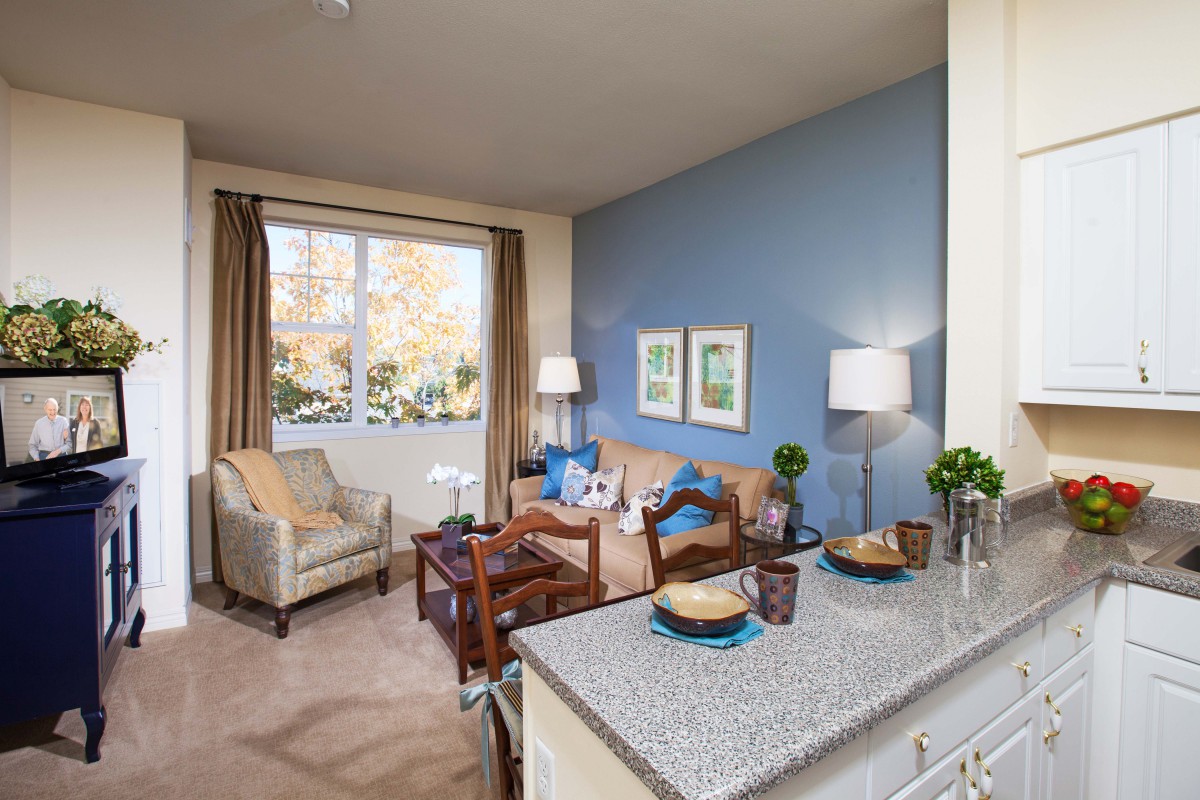 A cozy living room with a blue accent wall, featuring a comfortable sofa, armchair, and a small coffee table. The space is illuminated by natural light from the window and complemented by stylish lamps.