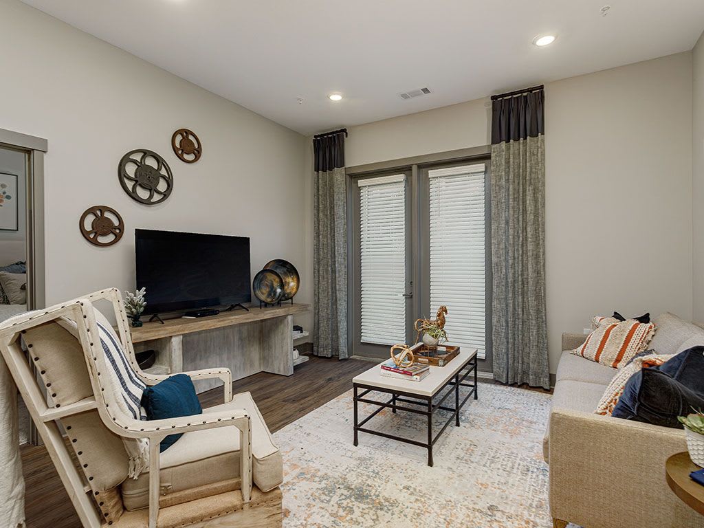 A cozy living room featuring a TV, sofa, armchair, and coffee table, with decorative items and curtains complementing the space.