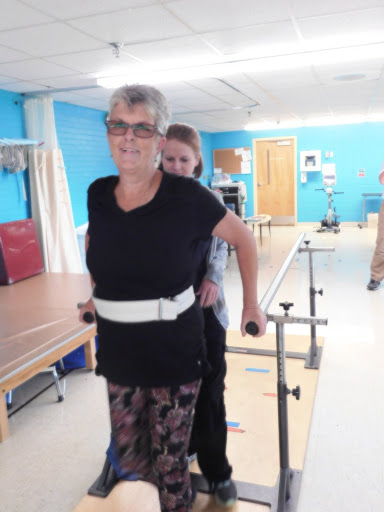 An elderly woman receiving assistance during physical therapy to improve her walking ability.