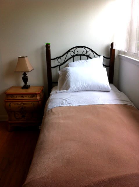 A neatly made single bed with a wooden headboard beside a nightstand with a lamp.