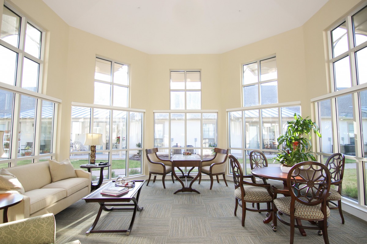 A bright and spacious living room with multiple tables, chairs, a sofa, and large windows.