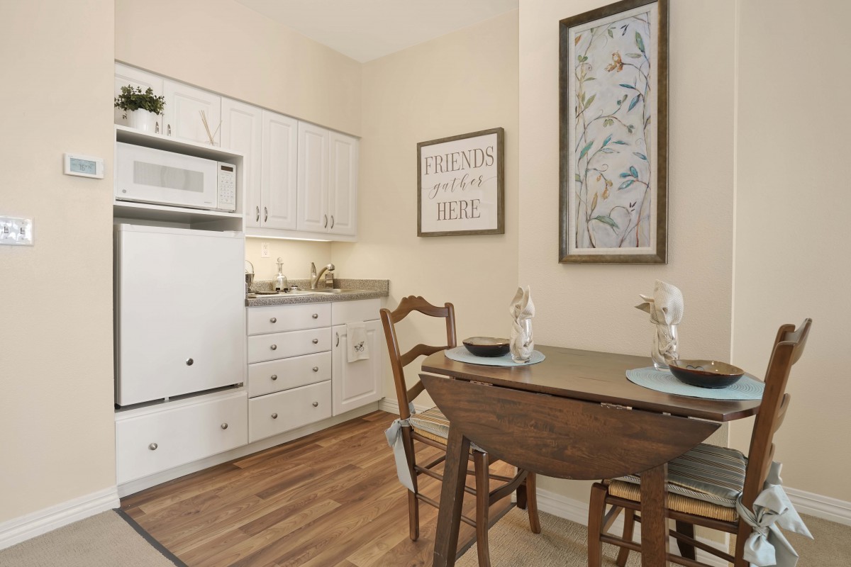 A cozy kitchen with a small dining setup, featuring white cabinets and wooden accents.