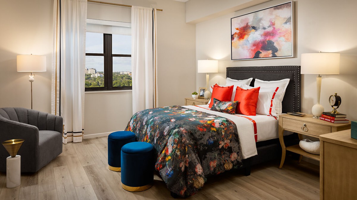 A stylishly decorated bedroom featuring a colorful bedspread, abstract artwork, and modern furniture with a view from the window.