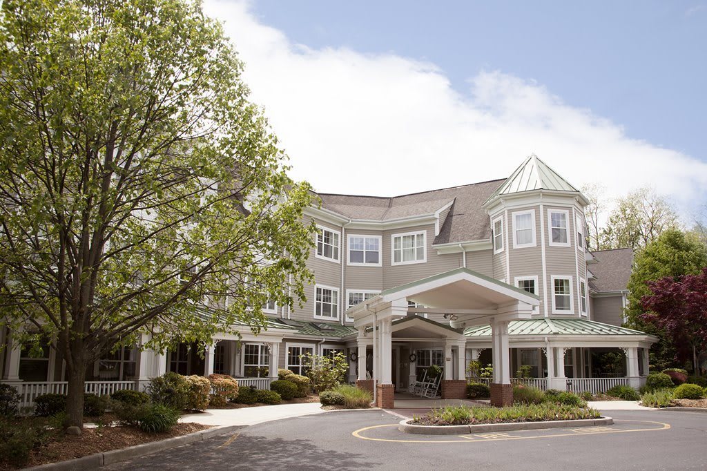 A three-story residential building with a covered entrance and surrounding greenery.