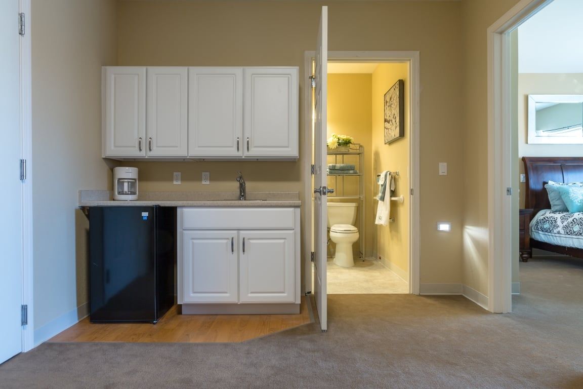 A compact kitchenette with white cabinets and an adjacent bathroom in a small apartment.