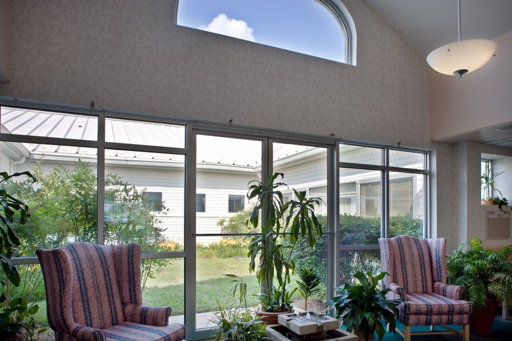A cozy living room with large glass doors, featuring a variety of plants and comfortable seating.