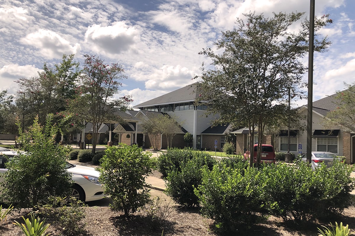 A sunny day with fluffy clouds over a landscaped area featuring a building and surrounding greenery.