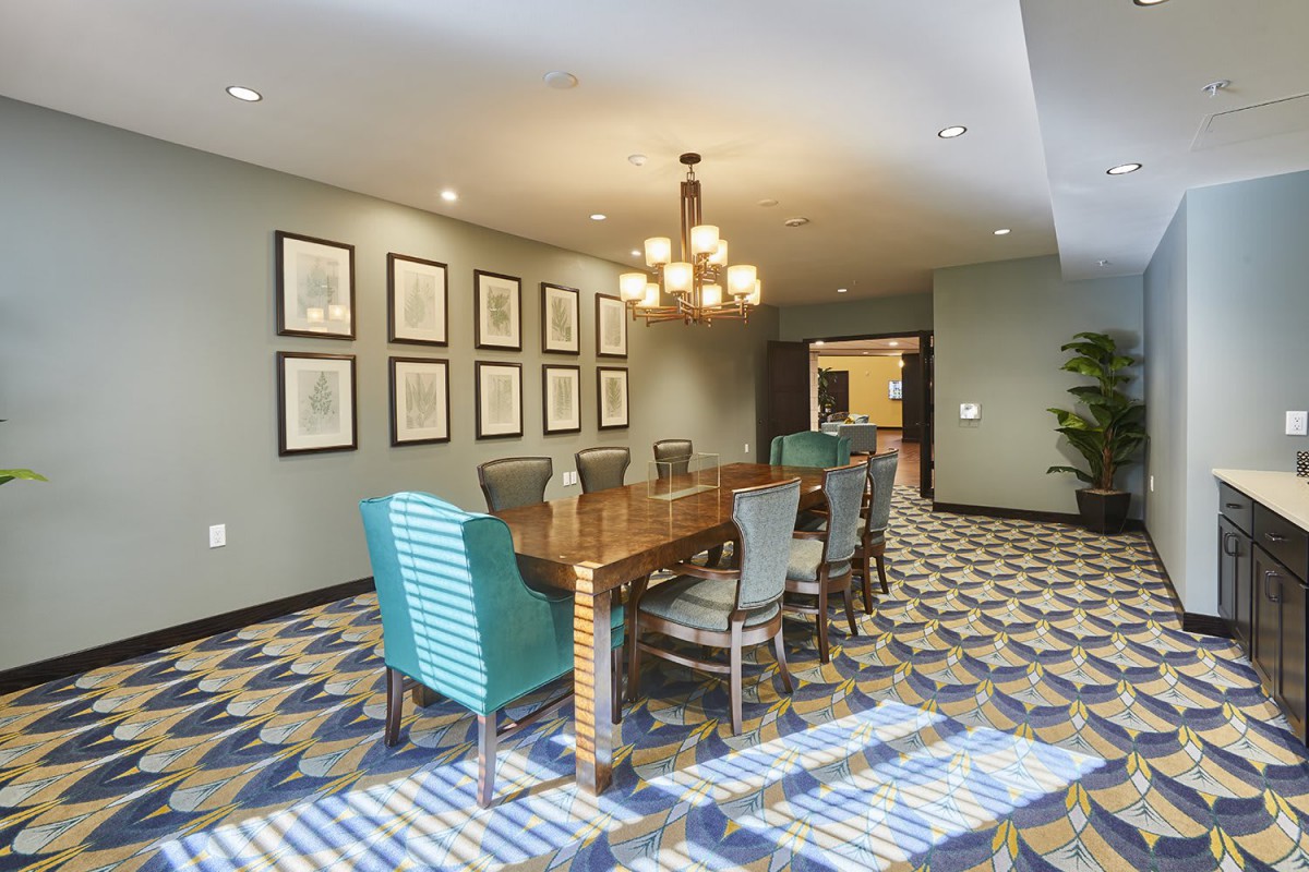 A modern conference room with a large wooden meeting table, elegant chandelier, and framed wall art.