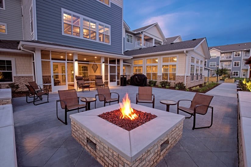 Cozy outdoor fire pit with seating at dusk in front of a modern building.
