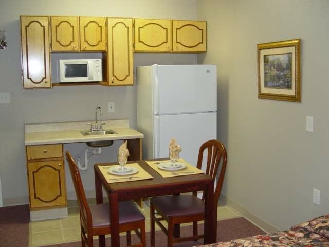 A small kitchen with a dining area, featuring wooden cabinets, a refrigerator, and a table set for two.