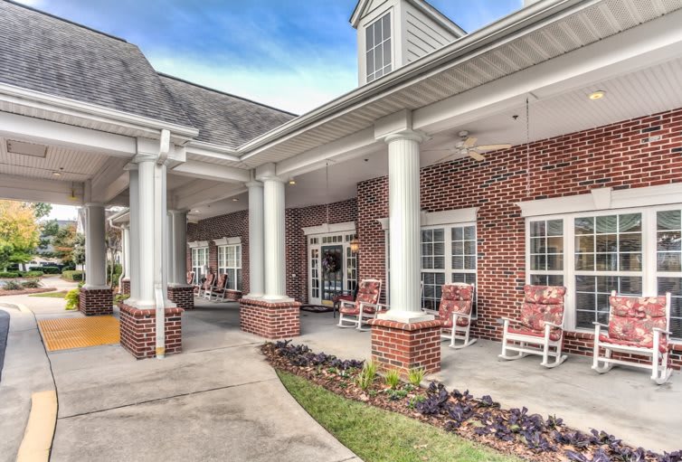 An elegant brick building with a porch featuring white columns and rocking chairs.