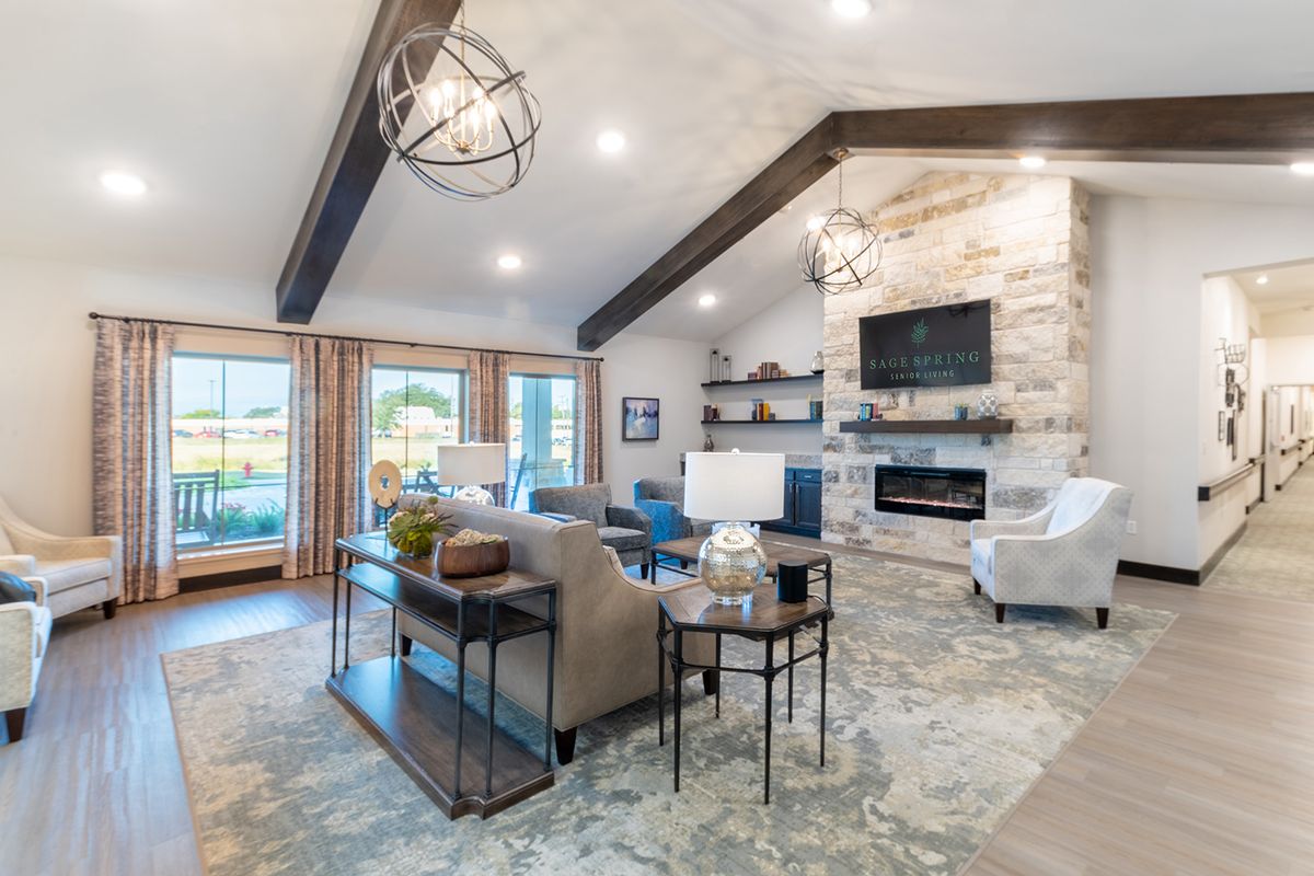 A modern living room featuring a vaulted ceiling with wood beams, a stone fireplace, and contemporary furnishings in neutral colors.