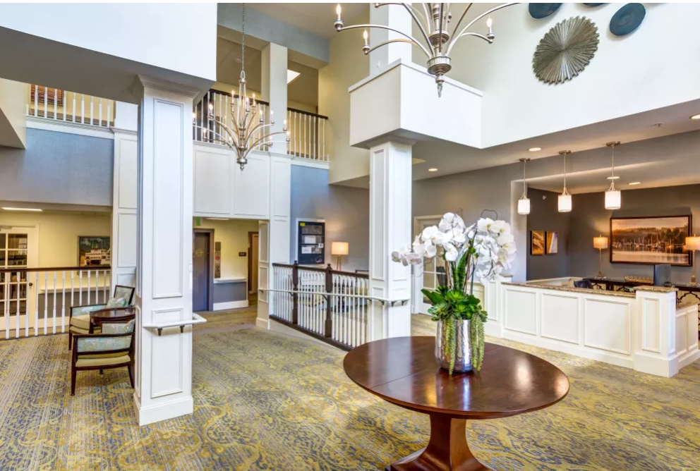 A spacious and elegantly decorated lobby with a large chandelier, polished wood table, and fresh orchids.