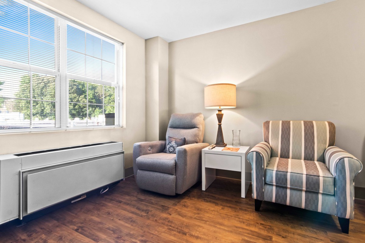 A cozy living room corner featuring a comfortable armchair and striped chair, with a side table and lamp by the window.
