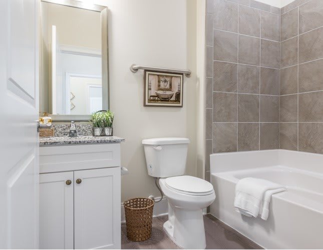 A modern bathroom with a toilet, bathtub, and sink featuring a large mirror and tile wall.