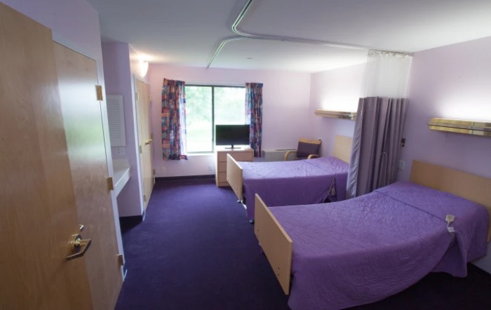 A hospital room with two beds and a small television near the window.