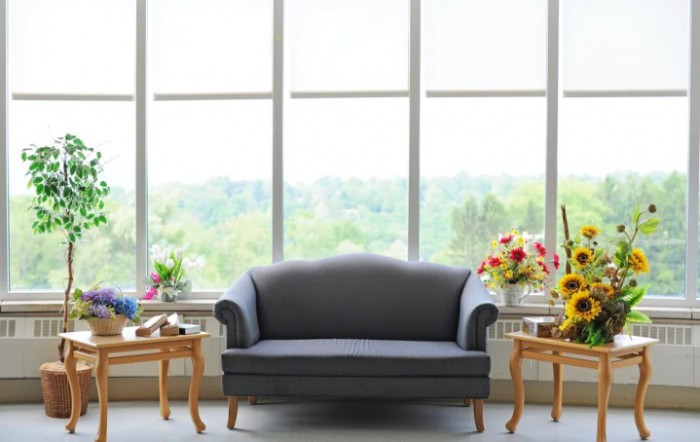 A cozy living room setup with a sofa, flanked by coffee tables and vibrant flower arrangements in front of large windows.