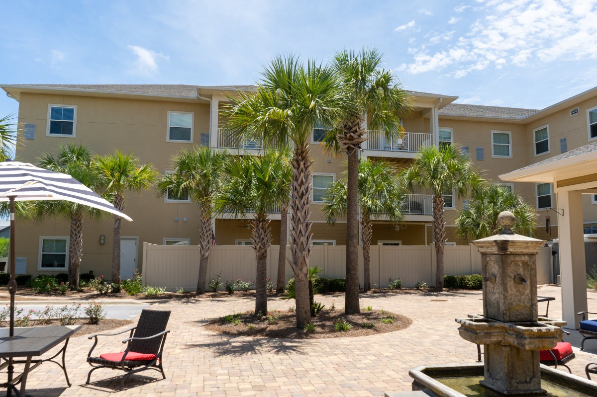 A sunny courtyard with palm trees in front of an apartment building.