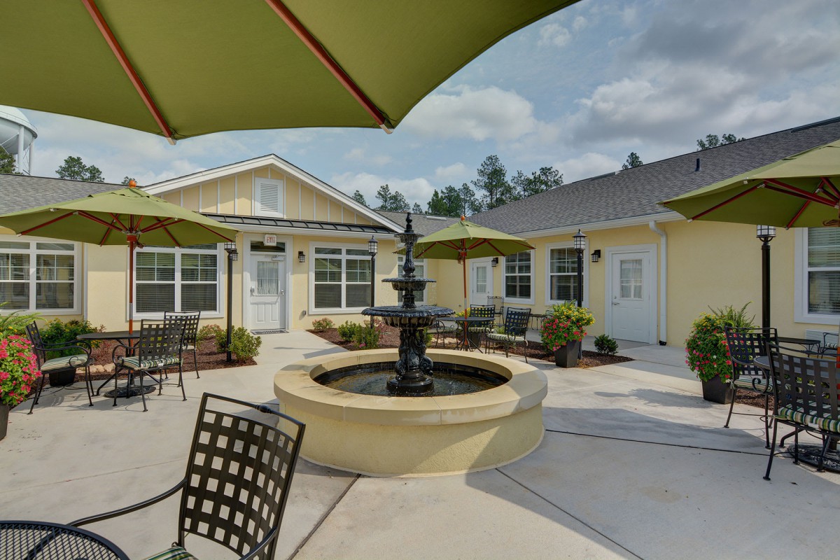 A serene courtyard featuring a central fountain, surrounded by outdoor seating with umbrellas on a sunny day.