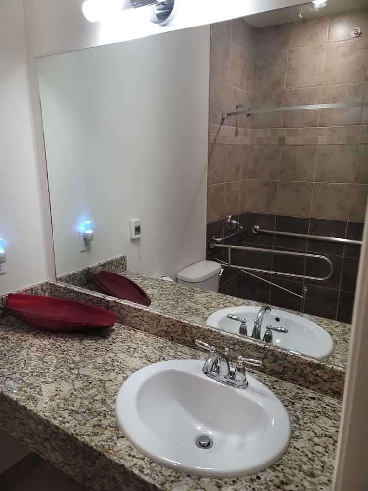 A modern bathroom featuring a granite countertop, a mounted mirror, and a neatly placed red towel next to the sink.