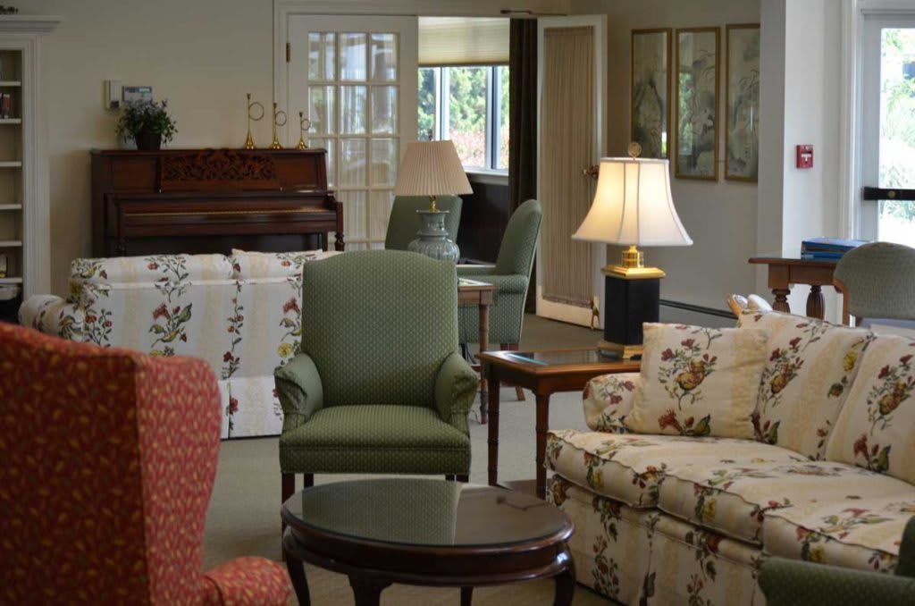 A cozy living room with a variety of seating options, including sofas and armchairs, and a piano in the background.