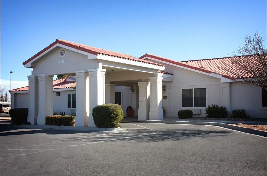 A commercial building with an entrance and parking area under a clear blue sky.