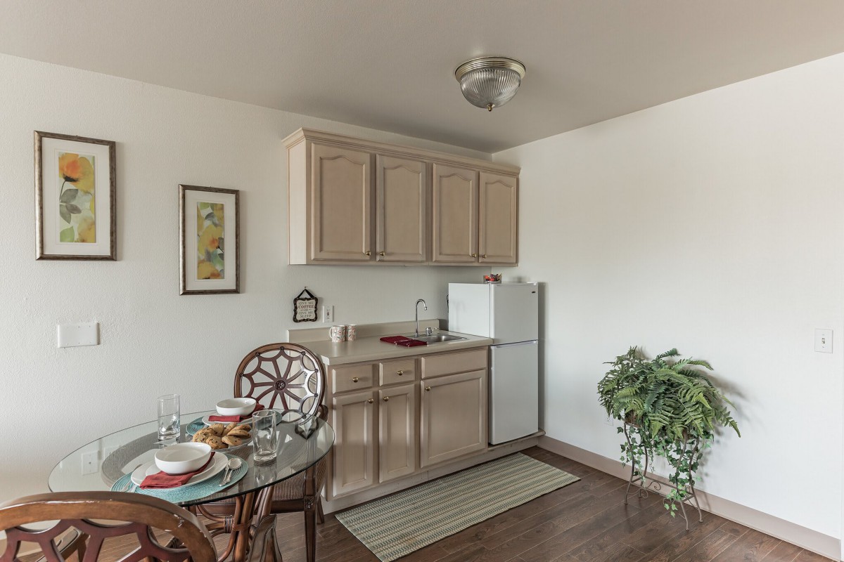 A small kitchen area with beige cabinets, a white refrigerator, and a dining table set for two.