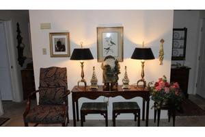 A well-decorated living room corner with a table, lamps, artwork, and chairs.