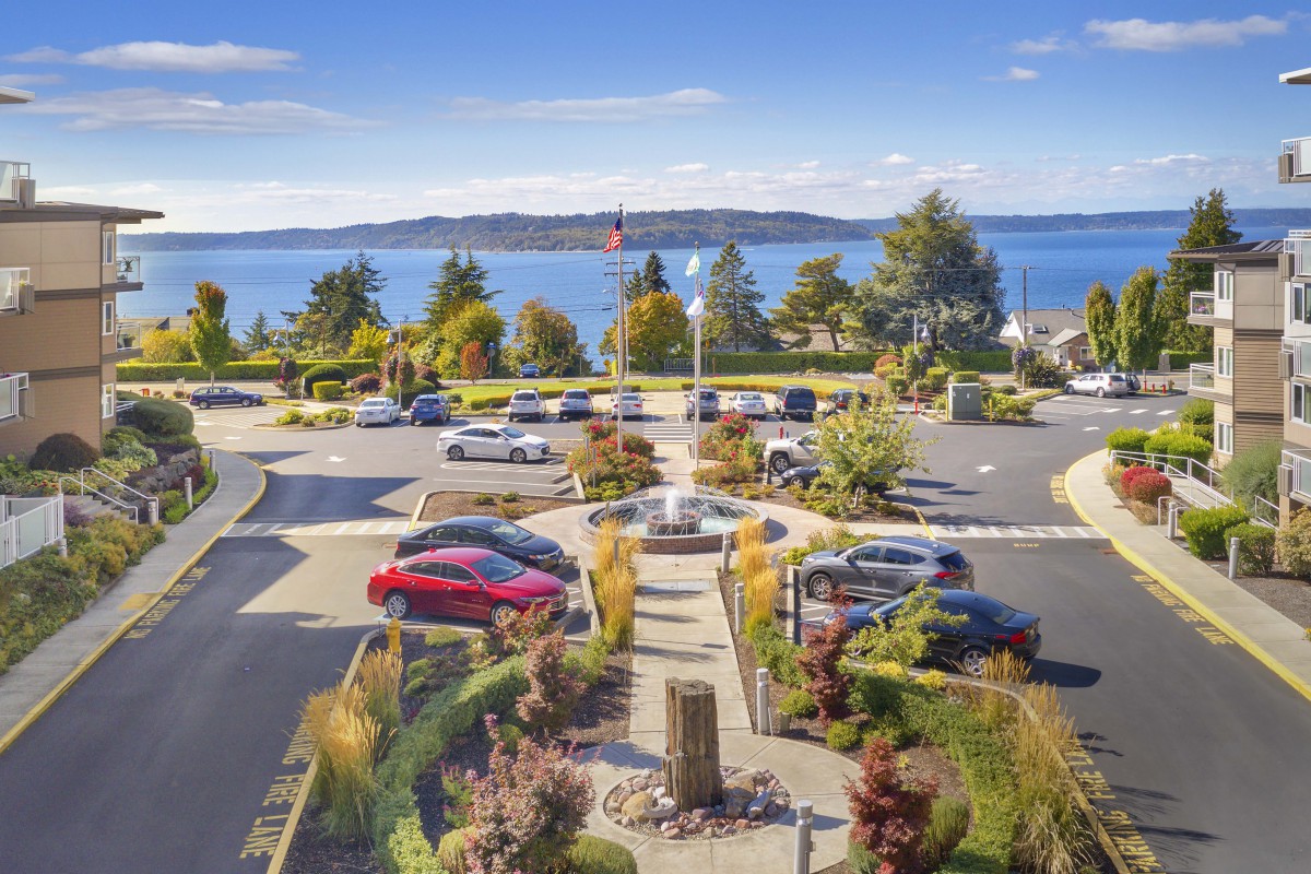 A scenic view of a parking lot overlooking the ocean, surrounded by gardens and trees.