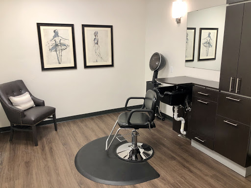 A minimalist hair salon featuring a stylist chair, mirror, and decorative artwork on the walls.