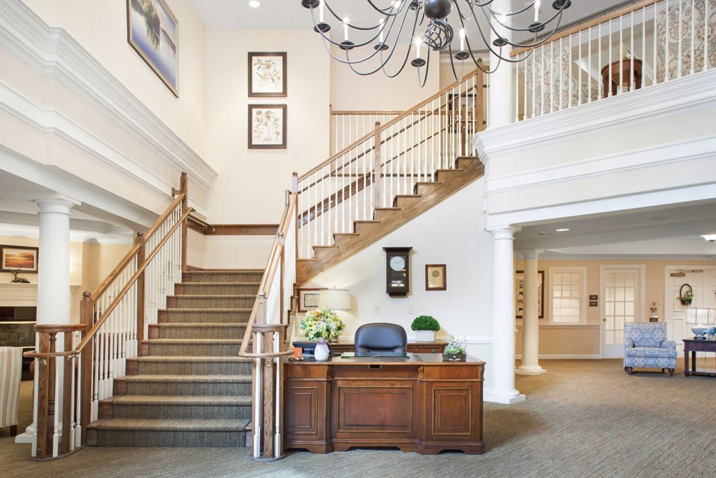 A well-lit interior space featuring a staircase and reception desk with a chandelier overhead.