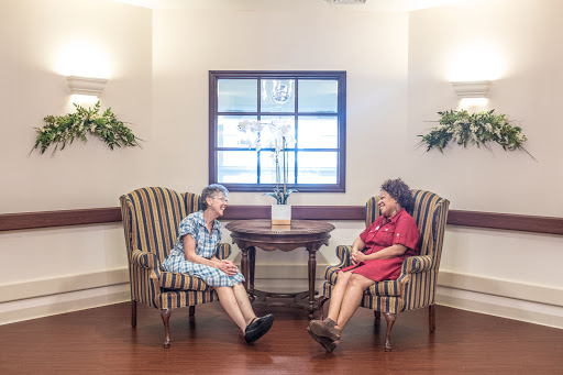 Two seniors engaging in a warm conversation in a cozy care facility.