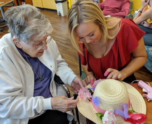 An elderly woman and a young woman are decorating a hat together indoors.