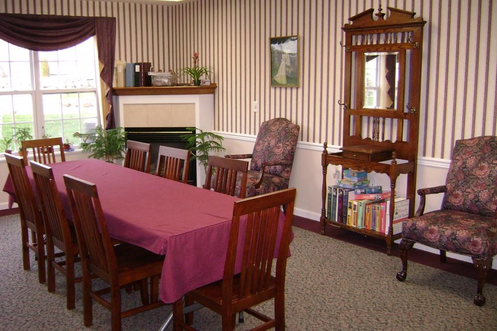 A cozy dining room with a table, chairs, and a bookshelf beside a decorated fireplace.