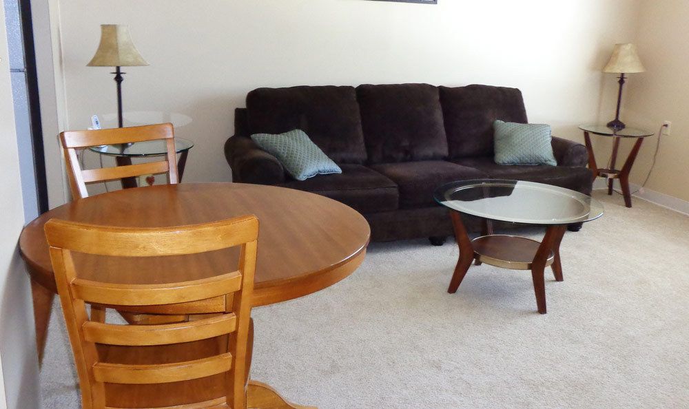 A cozy living room featuring a dark sofa, a stylish glass coffee table, and a wooden dining table with chairs.