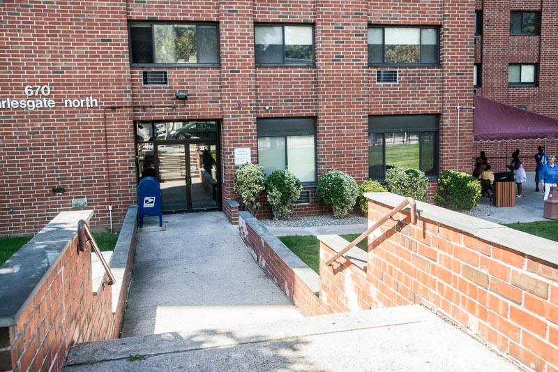 Entrance to a brick apartment building with stairs and sidewalk.