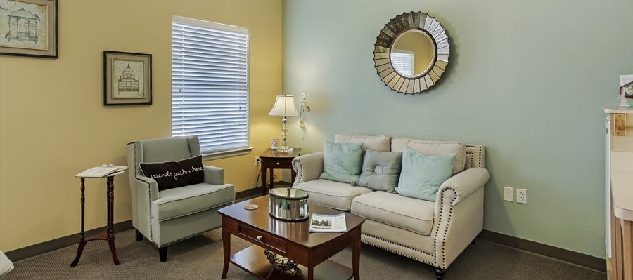 A cozy living room with a sofa, armchair, coffee table, and decorative mirror.