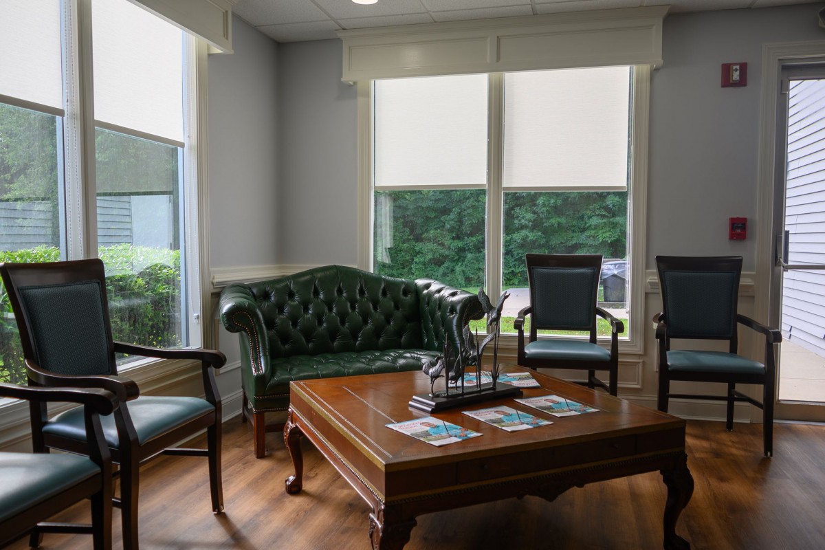 A well-lit waiting room with a sofa, chairs, and a coffee table near large windows.