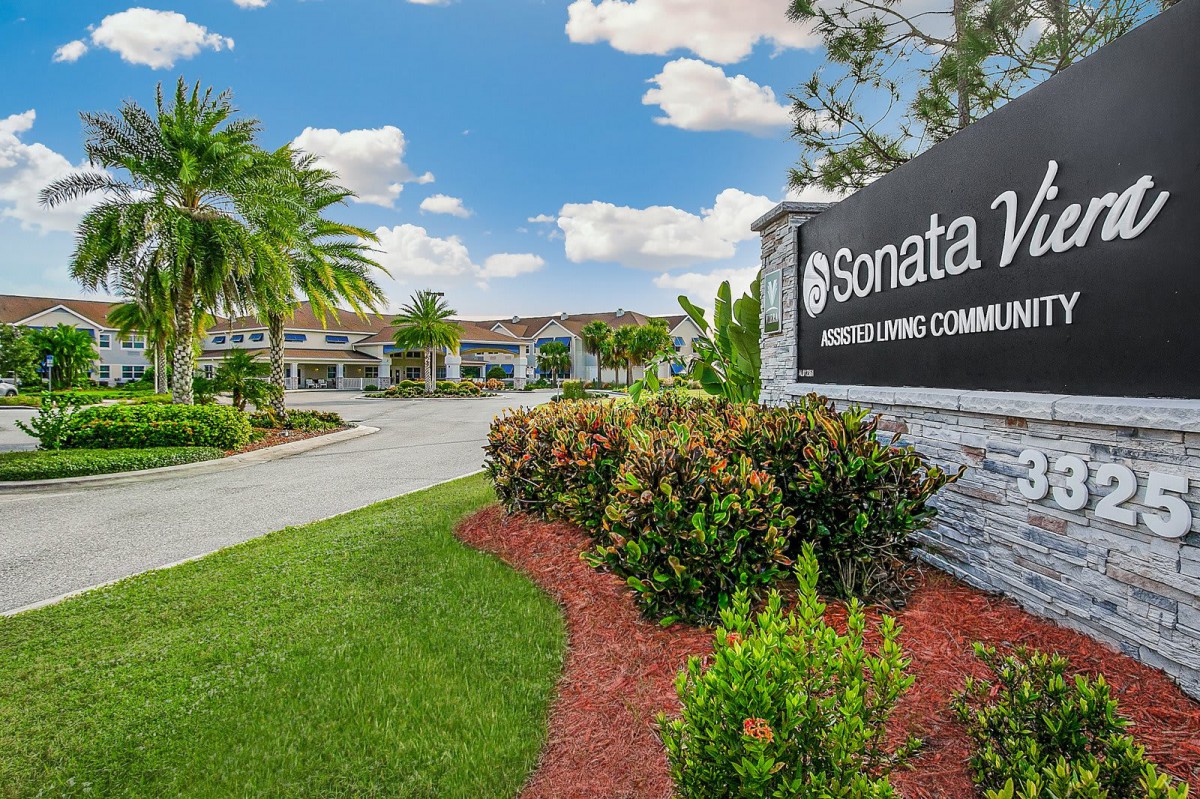 Entrance to a building complex with landscaped greenery and clear skies.