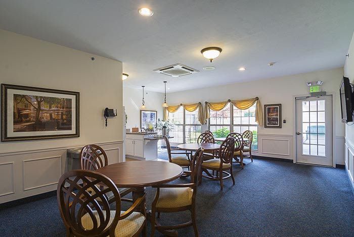 A cozy dining area with several round tables and chairs, adorned with warm lighting and large windows.