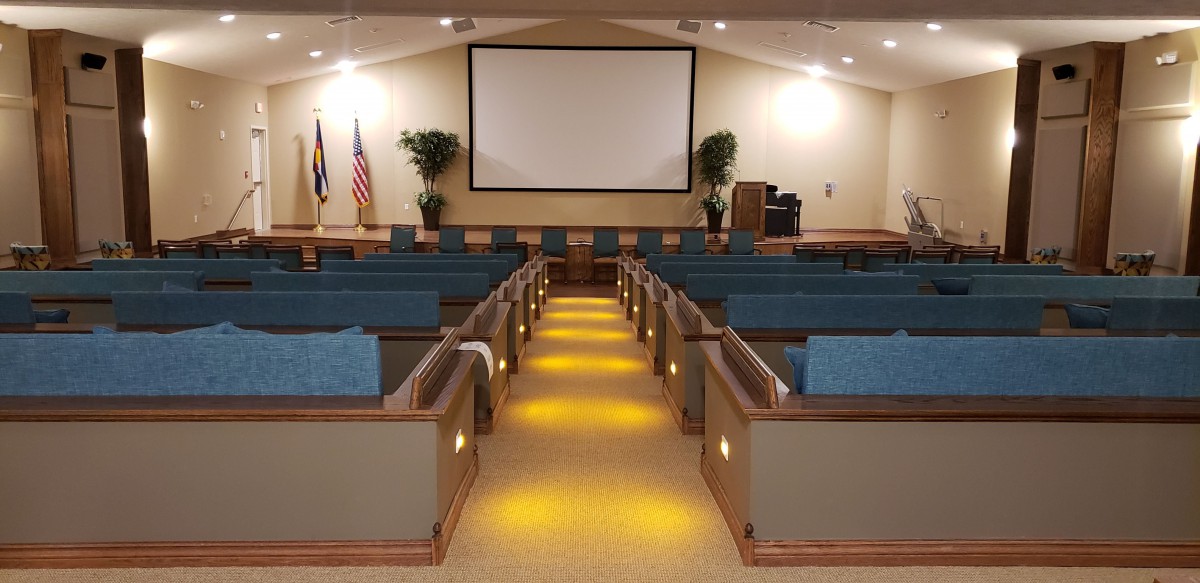 An empty auditorium with rows of cushioned seating facing a large projector screen in the front.