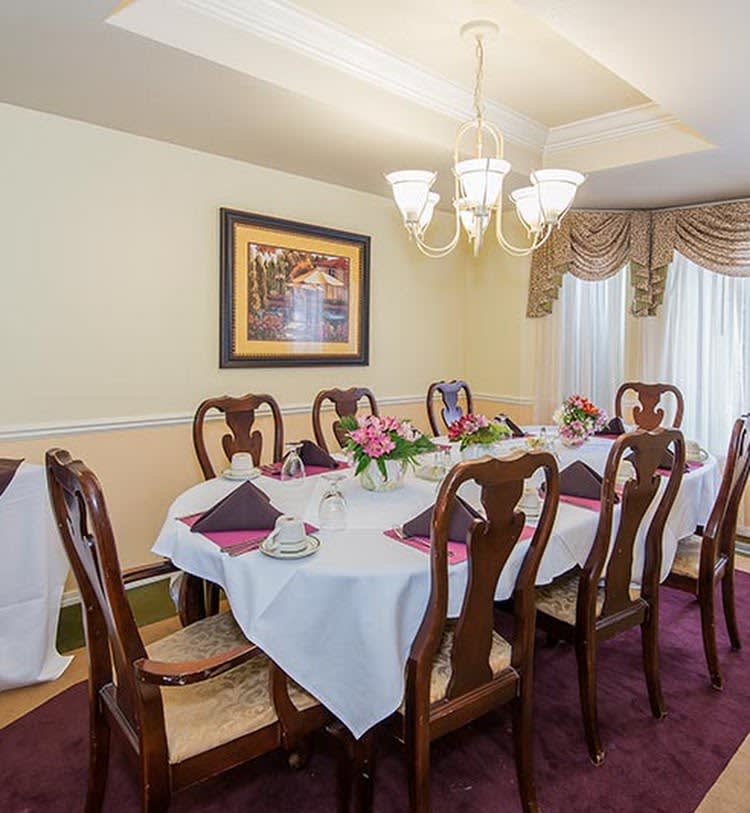 A well-decorated dining room with a large table set for a meal, featuring elegant chairs and a chandelier overhead.