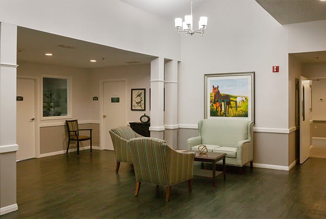 A cozy waiting area with a sofa and chairs arranged around a small table, illuminated by overhead lighting and adorned with wall paintings.