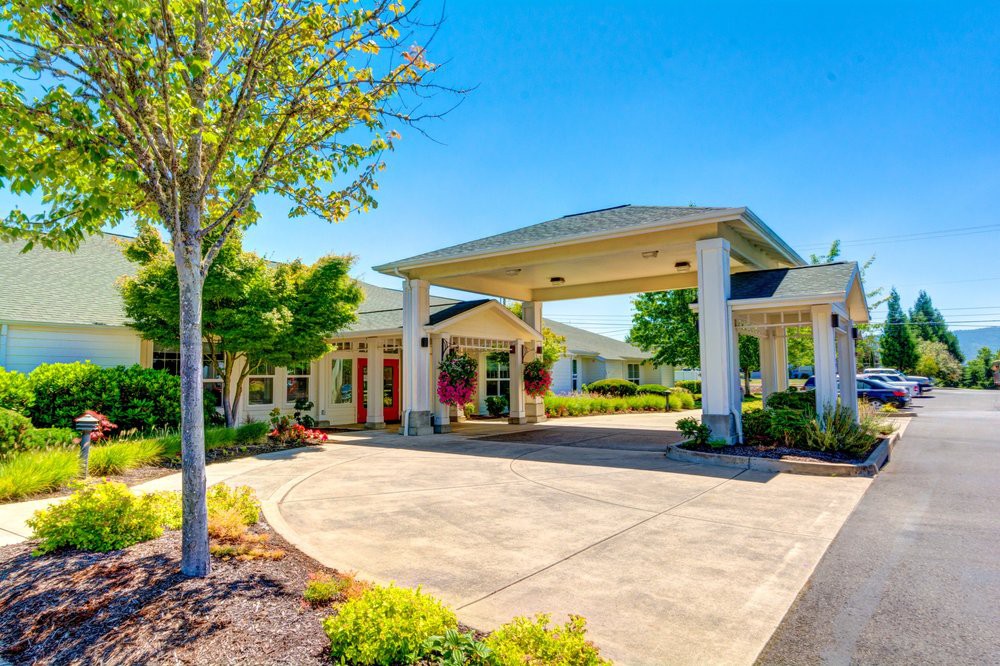 A sunny day view of a beautifully landscaped building entrance with a driveway.
