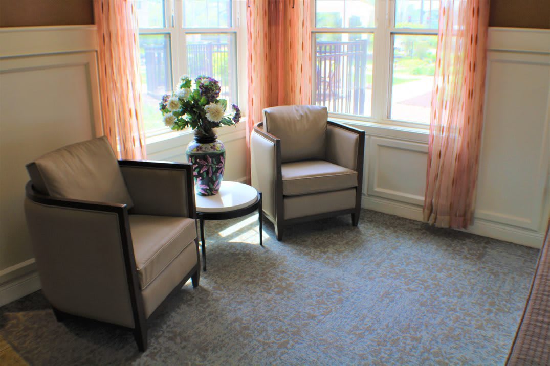 A cozy living room corner with two armchairs, a small table, and a vase of flowers by the window.