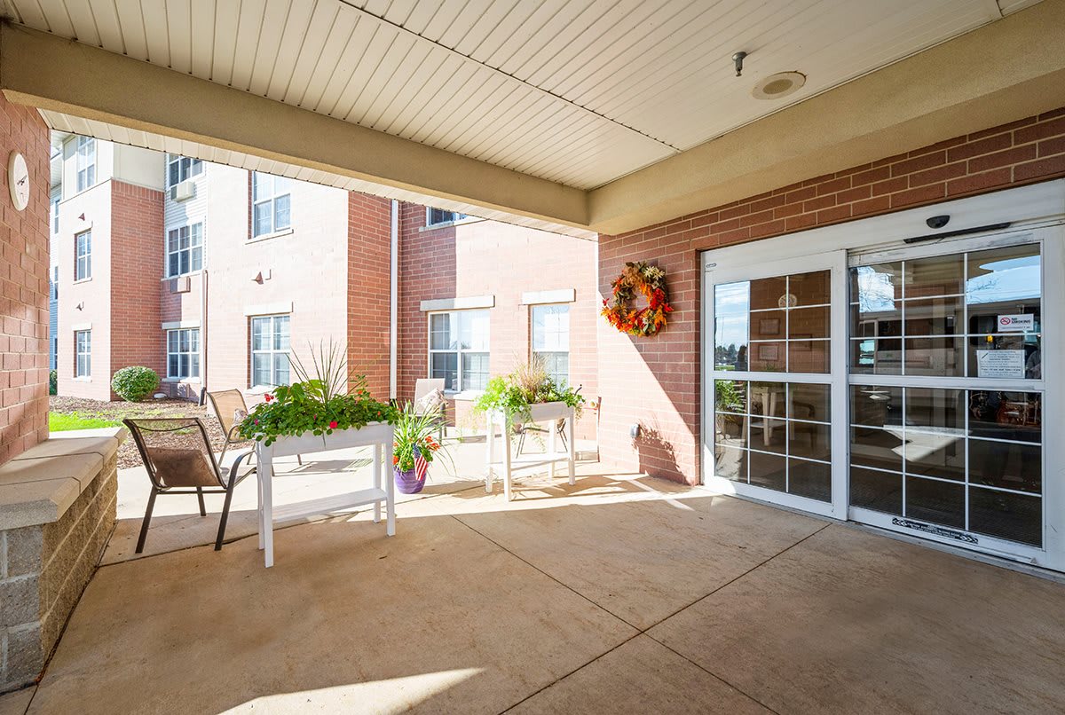 A sunny outdoor patio area with chairs and plants near a building entrance.