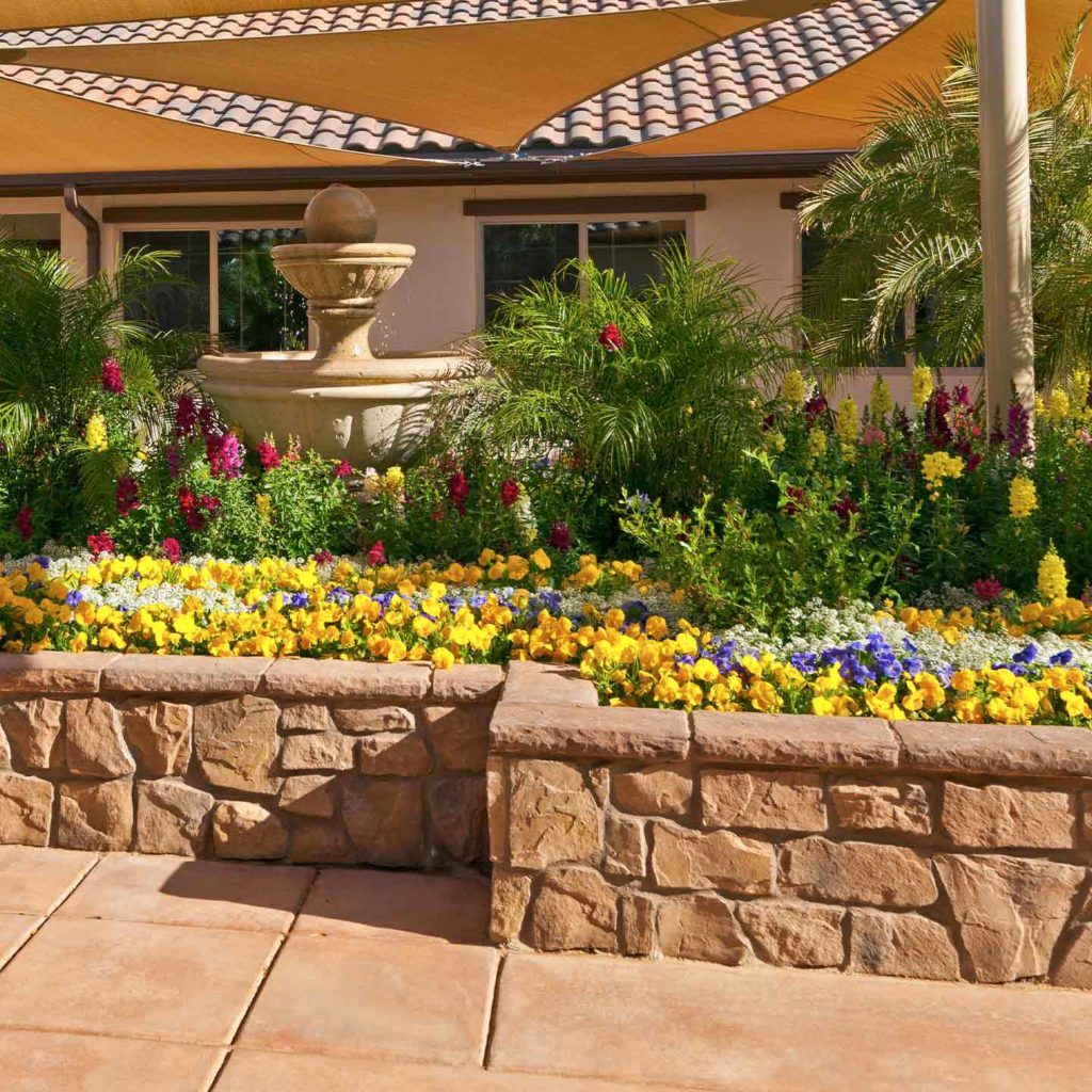 A beautifully landscaped garden with a variety of colorful flowers and a fountain on a sunny patio.