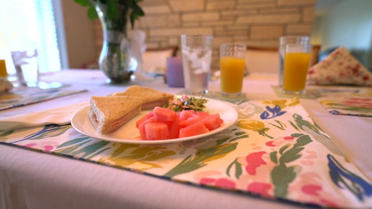 A breakfast setting with a sandwich, watermelon slices, and juice on a decorated table.