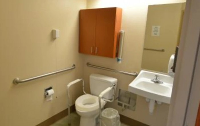 An accessible bathroom with a toilet, handrails, sink, and wooden cabinet.